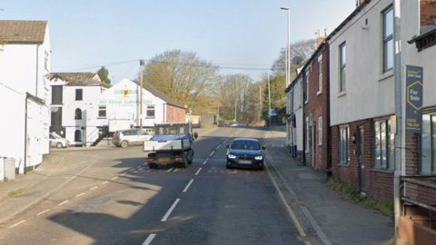 A street with white-fronted houses on both sides and a car and a small truck on the road