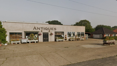 The exterior of the Suffolk Heritage and Antiques Centre in Old London Road in Copdock close to Ipswich. Plants have been set up outside the building and there is a large empty car park.