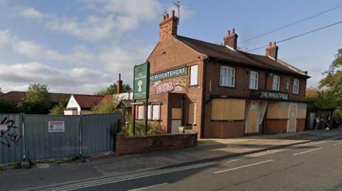 A Google Street View image shows the derelict Wheatsheaf pub. The doors and windows are covered with boards and there is graffiti on the side of the building