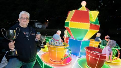 A man with a trophy next to his fairground ride boat