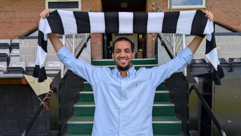 Ali Alhamad holding a Salisbury FC scarf over his head inside the stadium