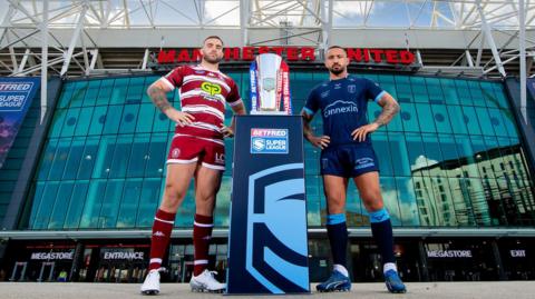 Stand-in Wigan captain Kaide Ellis and Hull KR skipper Elliot Minchella stand either side of the Super League trophy on the plinth outside Manchester United's Old Trafford stadium.