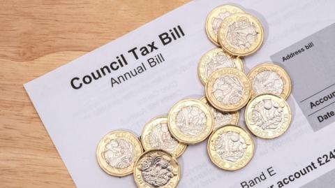 A photo of a council tax annual bill on a wooden surface. Several British £1 coins are laid on top of the piece of paper.