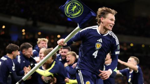 Scotland's Scott McTominay picks up a corner flag at the end of Scotland's win over Denmark at Hampden which sent Scotland to this summer's World Cup. Fellow players celebrate behind him.