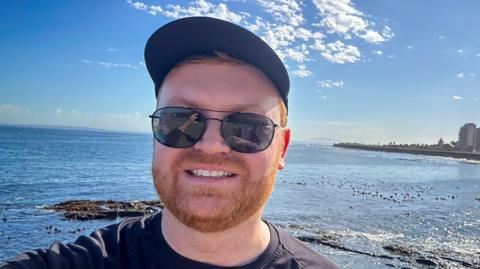 Ulrich Janse van Vuuren, with a cap and sunglasses, overlooking the ocean in South Africa