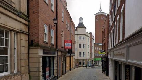 A narrow street in Shrewsbury with a cobbled surface and a clock tower in the distance