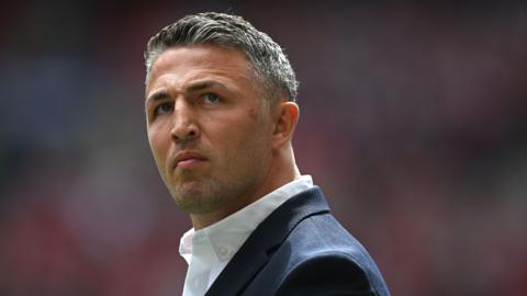 Warrington Wolves head coach Sam Burgess looking upwards. He is wearing a suit jacket and an open-necked shirt.