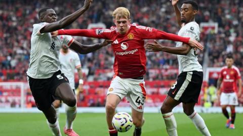 Toby Collyer taking the ball in between two Liverpool players