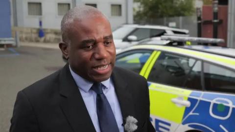 David Lammy talking in front of a police car