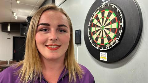 Samantha Lewis standing next to a darts board