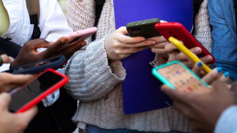 Young people stand in a circle looking down at phones they are holding