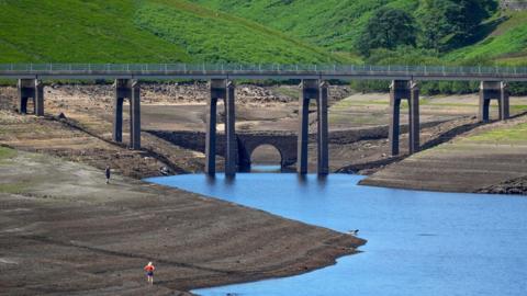 people walk on the dried up bed of Baitings Reservoir as the water level continues to drop on the eve of a hosepipe ban on July 10, 2025 in Ripponden, England. 