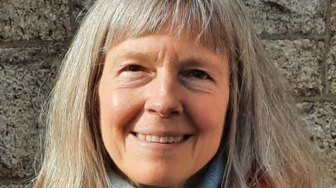 The Reverend Dr Katherine Meyer - a close up shot where she is looking straight at the camera and smiling. She has long silver-blonde hair