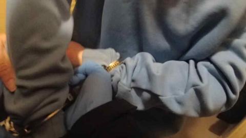 A person in a blue jumper being placed in handcuffs