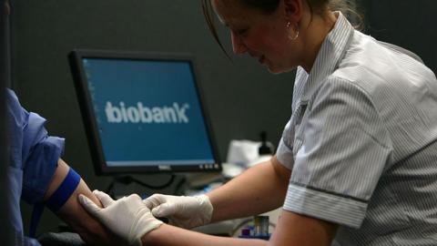 Nurse taking blood from person as biobank logo appears on screen in background.