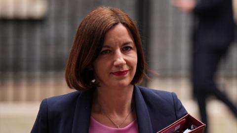 Bridget Phillipson leaves 10 Downing Street. She is wearing a navy blazer and a pink blouse and is holding a red binder.