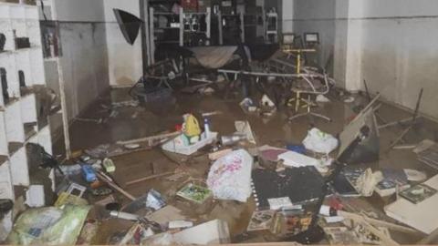 A basement full of household items and photography equipment is waterlogged with brown water. The room has a large amount of water on the floor. 