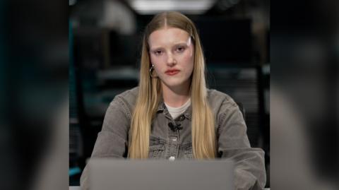 Morven McKinnon - a young woman with long straight blonde hair, sitting at a desk with an open laptop in front of her