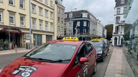 The photo shows a street with three taxis lined up at taxi rank.