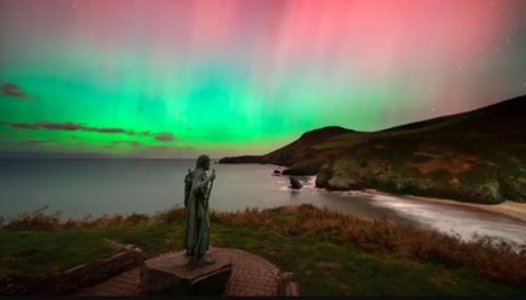 St. Crannog's statue is watching over the shoreline underneath the Northern Lights which is showcasing different colours such as green, pink and blue in the sky.