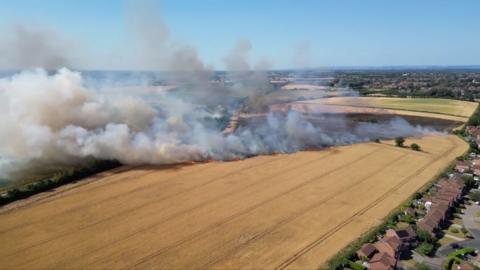 A drone shot of smoke rising from a farm field.