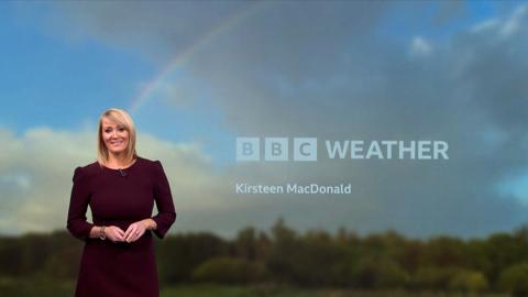 Woman wearing burgandy dress, with blue sky and rainbow in the background.