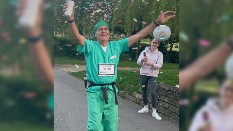 Mark Hillyard finishes his challenge in green scrubs, is smiling with arms in the air and confetti has been thrown