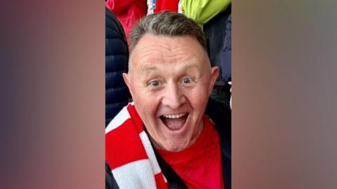 Harvey Trout, wearing a red and white scarf, smiling broadly at the camera