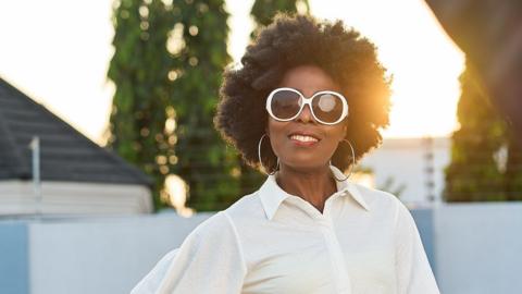 Irene wears large white rimmed sunglasses and a white long sleeved shirt.