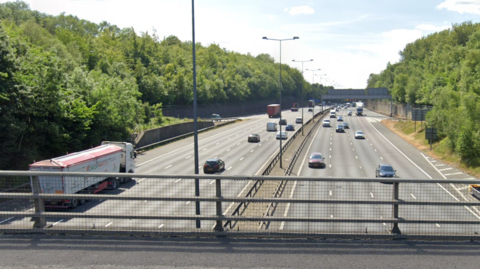 A motorway seen from a motorway bridge. Cars and vans are travelling in both directions.