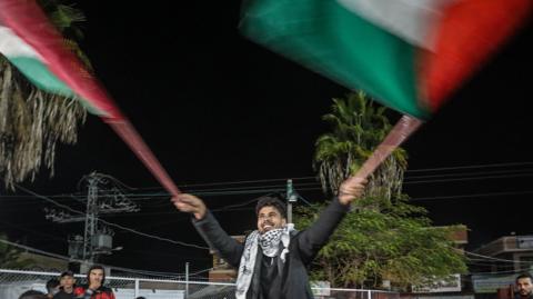 Palestinian man waving two flags in celebration