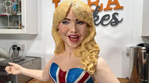 A cake in the shape of Sabrina Carpenter with her arms outstretched and she's wearing a union jack bodice