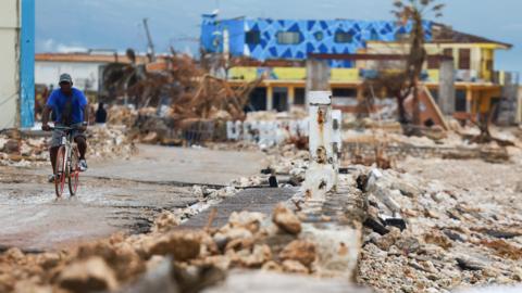 A man rides a bicycle along a concrete road, past damaged buildings in the aftermath of Hurricane Melissa, in Black River, Jamaica,