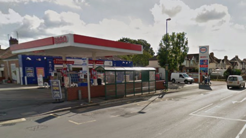 An Esso garage is by the side of a road with residential homes in a row behind the garage from a Google streetview screenshot