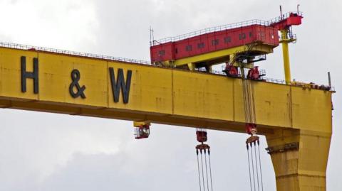 Twin shipbuilding gantry cranes in Titanic quarter. They are both yellow with H&W in black lettering printed across the top. The sky is very blue.