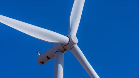 Close up of a wind turbine in field against a blue sky.