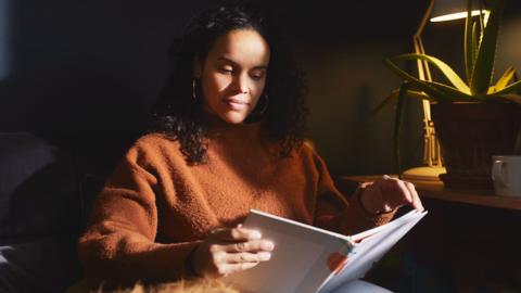 A woman sat on the sofa with her dog looking into a notebook.