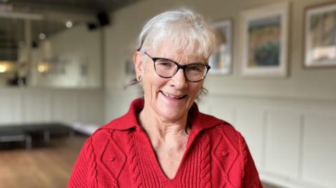 Festival president Hilary Cox inside an empty room at The Cliftonville Hotel in Cromer. She has short grey hair, dark glasses and is wearing a red jumper.