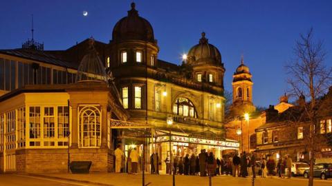 Buxton Opera House - a highly elaborate theatre building - lit up at night with queues outside the front entrance