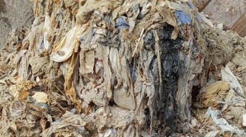 A fatberg seen with different items such as sanitary products and wet wipes in a huge mass. It is brown and yellow in colour. 