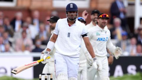 England's Emilio Gay (centre) reacts after being caught out by New Zealand's Daryl Mitchell on day one of the first Rothesay Test match at Lord's, London. He is holding a bat in one arm, has a helmet on and is wearing white. He has a black armband on.