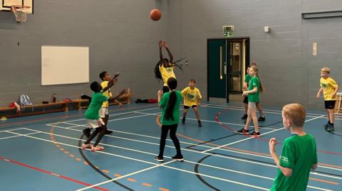 Children playing basketball wearing green or yellow t shirts in a sportshall