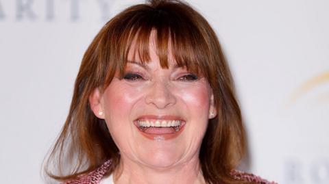 A close-up of a laughing Lorraine Kelly taken at an event. She wears glamorous makeup and a pink tweed jacket