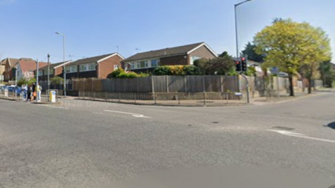 The corner of a road junction. There are road marking showing turning lanes on the ground and a built up area of houses. 