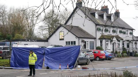 A police officer stands outside the Three Horseshoes pub in Knockholt.