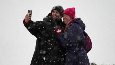 A man and a woman take a selfie as snow falls