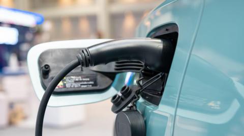 A close-up image of a large black plug plugged into the charging point of a blue electric car