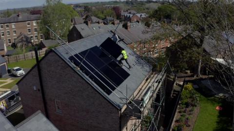 People on scaffolding installing solar panels to a house's roof.
