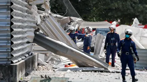 Rescuers in dark blue uniforms inspect the rubble of an earthquake in Japan's Kumamoto prefecture