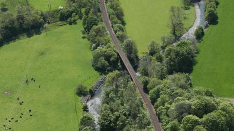 An aerial view of the Stranraer to Ayr railway line passing over a river with trees and fields around it